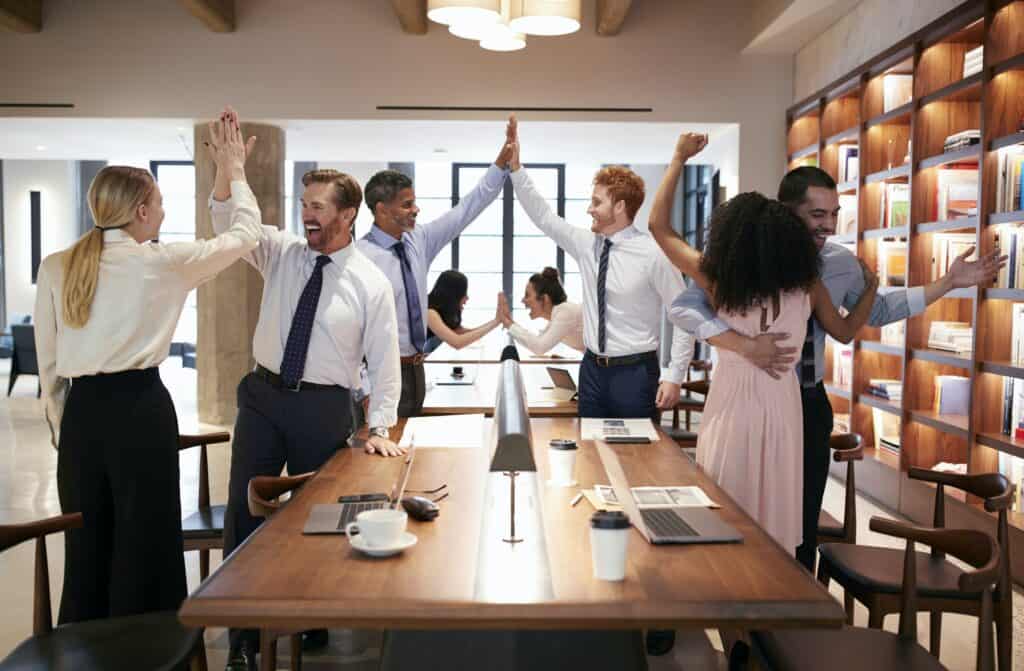 Six colleagues celebrating success in an open plan office