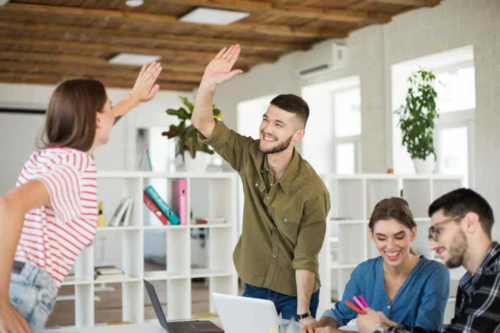 Young joyful man in shirt happily giving high five to colleague