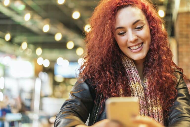 Young woman sitting in trendy cafe writing with her mobile phone.